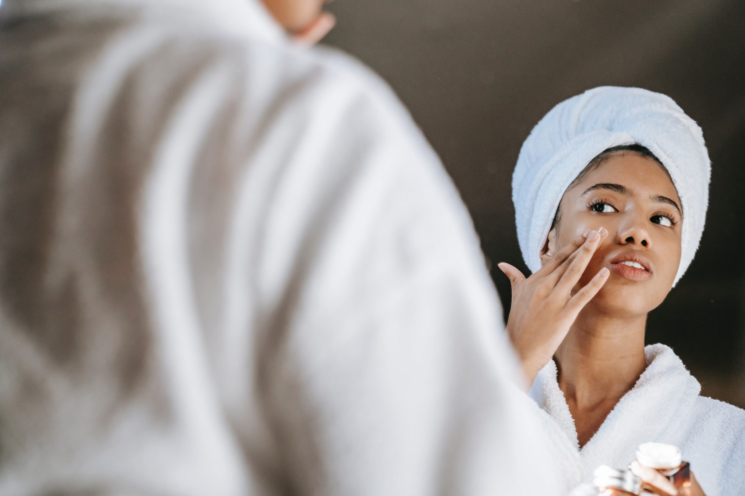 Woman looking herself in the mirror while applying her sunscreen before getting ready for the day as explained in this sunscreen guide